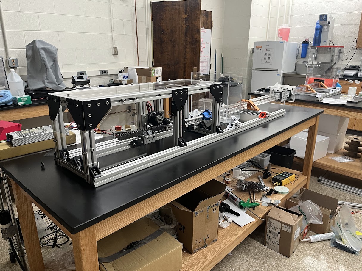 Assembled senior design oscillatory flume with an aluminum extrusion frame and rack-and-pinion drive on a lab bench.